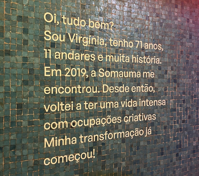 Parede do Edifício Virginia na exposição da Semana de Design 2023, em São Paulo, com uma frase estampada de apresentação das atividades desenvolvidas atualmente no prédio em parceria com a Somauma.